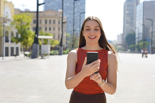 Brazilian woman using mobile phone app on sunny day in Sao Paulo downtown, Brazil