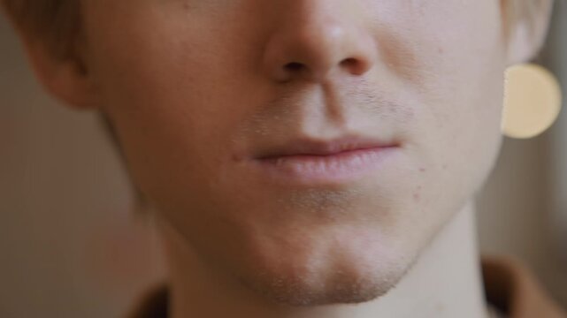 Close up of man using dental floss to clean teeth with steady hand and visible skin texture in soft indoor lighting. Dental string is manipulated near mouth area focusing on oral hygiene