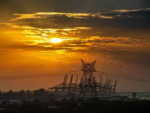 View of industrial port cranes and electrical power lines silhouetted against a vibrant golden sunset sky in Dubai, Dubai, United Arab Emirates.