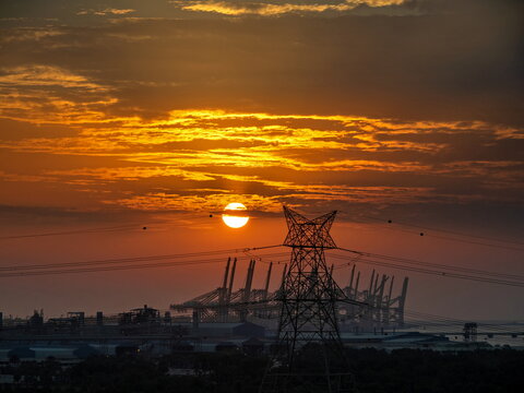 View of a sunset over an industrial port area with power lines and cranes in the distance in Dubai, Dubai, United Arab Emirates.