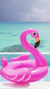 Summer vacation fun vertical crop of pink flamingo swimming pool toy float floating on infinity luxury resort pool with blue ocean background.