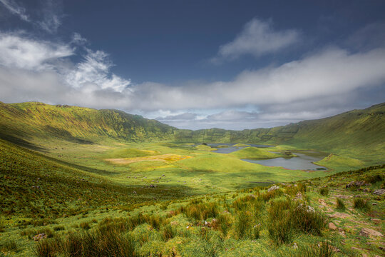 Corvo, Azores, Portugal Lush green hills surround calm lake under blue sky. Gentle slopes covered in vibrant vegetation. Scenic valley offers peaceful natural beauty. Perfect for travel or nature-them