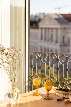amber gold vintage goblet wine glass and olives on a table next to linen napkin and wine opener with balcony and city views in late afternoon with glass vase of wildflowers 