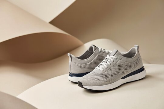 Pair of modern grey knit sneakers on a minimalist abstract beige background