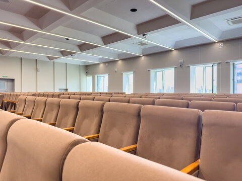 Modern conference room with rows of beige upholstered chairs and large windows