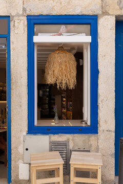 street view of blue trim window of small restaurant in Lisbon, Portugal with large rattan lamp and two stools outside