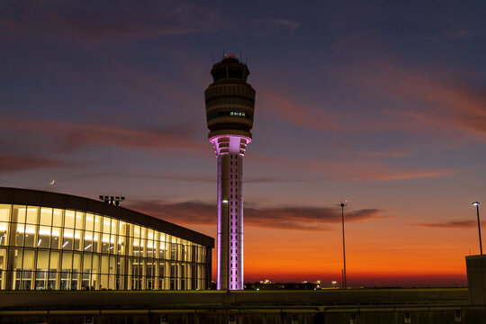 View of the Hartsfield-Jackson Atlanta International Airport air traffic control tower illuminated against a vibrant sunset sky in Atlanta, Georgia, United States.