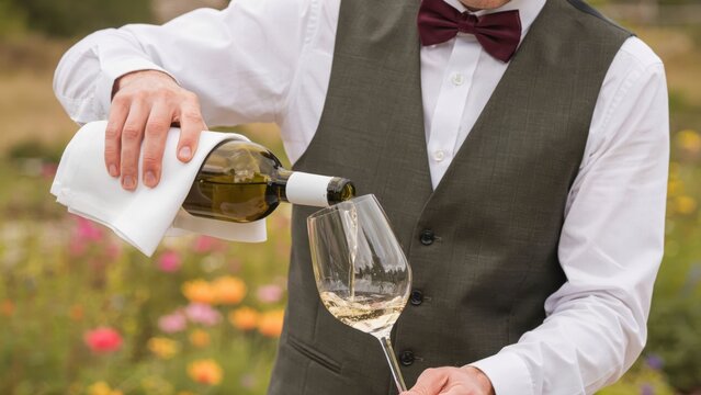 Waiter pouring white wine into a glass in a garden setting