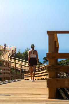View of a woman walking along a wooden boardwalk overlooking the ocean in Portugal.
