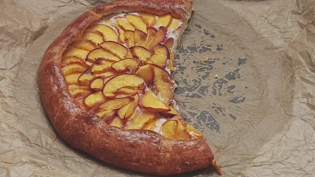 Freshly baked homemade fruit pie rotating on parchment paper. Delicious rustic peach galette with a flaky crust and sweet filling
