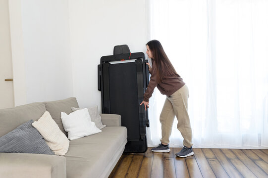 Mujer guardando cinta caminadora plegable en espacio peque&ntilde;o del hogar