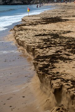 View of beach erosion showing a steep sand cliff and seaweed deposits along the shoreline in Cascais, Lisbon, Portugal.