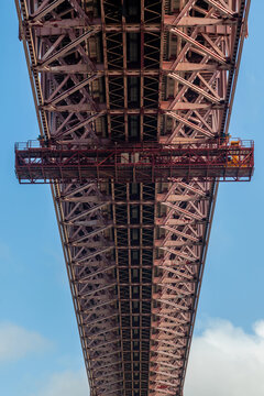 View of the intricate steel truss structure of the Ponte 25 de Abril bridge against a clear blue sky in Lisbon, Lisbon, Portugal.