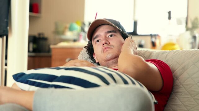 Bored young millennial man laying on the sofa thinking