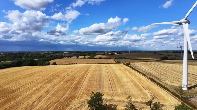 Aerial view of the Burton Wold wind farm turbine 1 standing in golden wheat fields under a blue sky with clouds in Burton Latimer, England, United Kingdom.