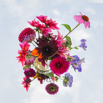 abstract floral art arrangement with dahlia flowers in glass vase on mirror with sky
