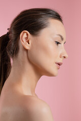 Fototapeta premium Profile of a young woman with smooth skin and subtle makeup on a pink background
