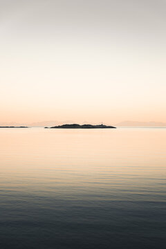 View of the calm sea and a small island in the Lofoten archipelago at sunset in Nordland, Norway.
