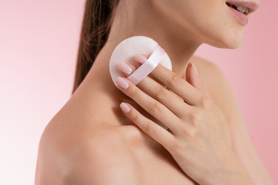 Woman applying powder with a soft puff on her shoulder and neck