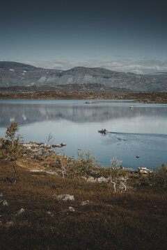 View of Vassijaure lake with a small boat carrying people on the calm water, surrounded by rugged mountains and tundra landscape in Riksgransen, Norrbotten County, Sweden.