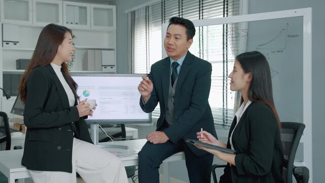 Business professionals having a strategic discussion in a modern office with a marketing budget presentation displayed on a monitor. Team members exchange ideas and evaluate business performance toget