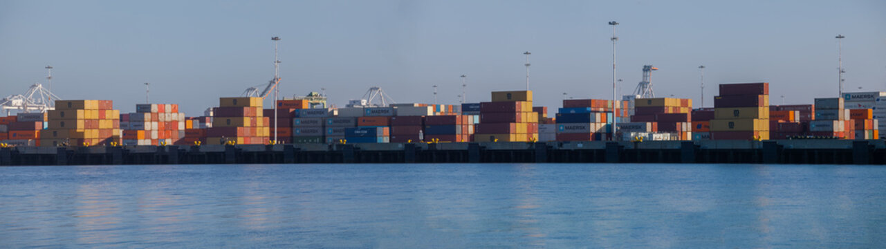 Pano of multicolored cargo containers arranged along the dock as port cranes rise overhead during routine shipping operations in Oakland, California