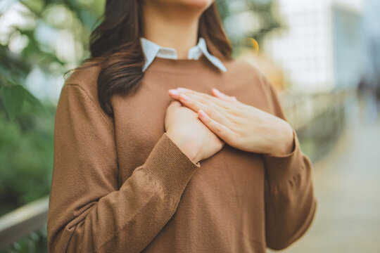 Woman placing hands over heart, expressing gratitude, appreciation and heartfelt emotion outdoors