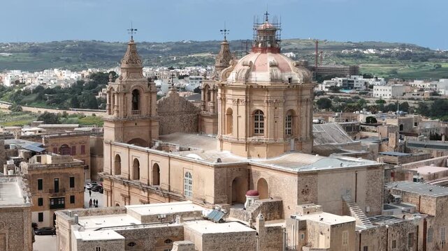 cathedral dome mdina st pauls twin bell towers baroque architecture rooftops malta scaffolding restoration aerial drone close orbit ochre limestone spire cross religious landmark