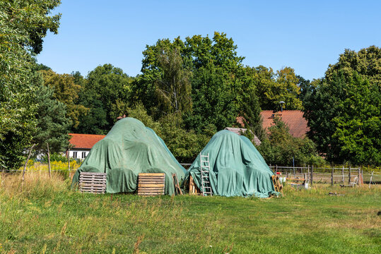 Kegelf&ouml;rmiger Stapel von Heu und Stroh der mit einem landwirtschaftlichen Abdeckvlies gesch&uuml;tzt ist, Bauernhof in der Uckermark, Brandenburg, Deutschland