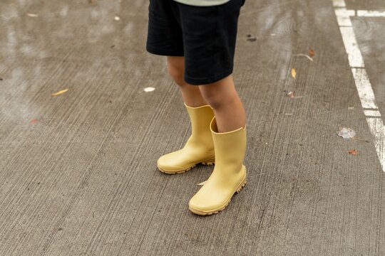 Child Wearing Yellow Rain Boots on Wet Pavement