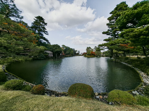 View of Kenrokuen Garden featuring a tranquil pond surrounded by manicured pine trees and lush greenery in Kanazawa, Ishikawa, Japan.