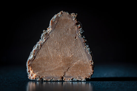 Closeup macro shot of chocolate truffle candy sliced in half showing its smooth rich ganache filling structure isolated on dark moody background