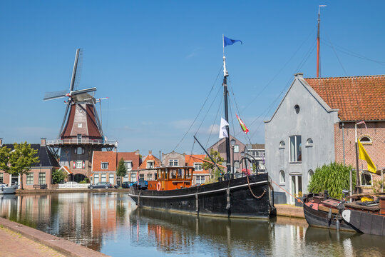 Historic black ship near a traditional windmill along a sunny canal in Meppel, Netherlands