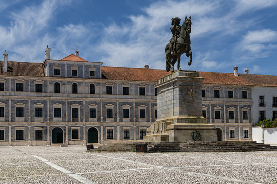 View of the Ducal Palace of Vila Vicosa with its marble facade and the equestrian statue of King John IV in the foreground under a blue sky in Vila Vicosa, Distrito de Evora, Portugal.