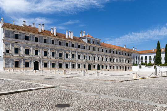 View of the historic marble facade of the Ducal Palace of Vila Vicosa overlooking the expansive cobblestone square under a clear blue sky in Vila Vicosa, Distrito de Evora, Portugal.
