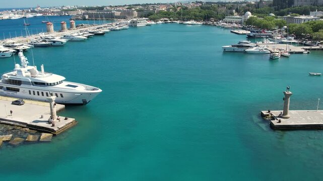 Aerial drone footage of Mandraki Harbour in Rhodes, Greece, featuring the famous Doe Statues, yachts and boats moored in the historic harbour. Bird's-eye view of the waterfront, Mediterranean Sea 