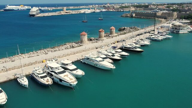 Aerial drone footage of Mandraki Harbour in Rhodes, Greece, featuring the famous Doe Statues, yachts and boats moored in the historic harbour. Bird's-eye view of the waterfront, Mediterranean Sea 