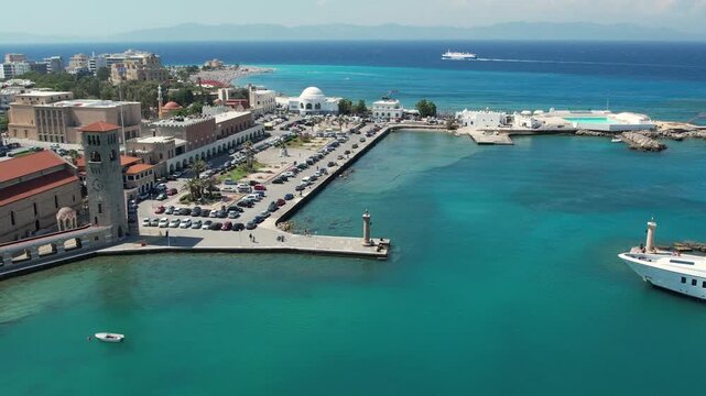 Aerial drone footage of Mandraki Harbour in Rhodes, Greece, featuring the famous Doe Statues, yachts and boats moored in the historic harbour. Bird's-eye view of the waterfront, Mediterranean Sea 