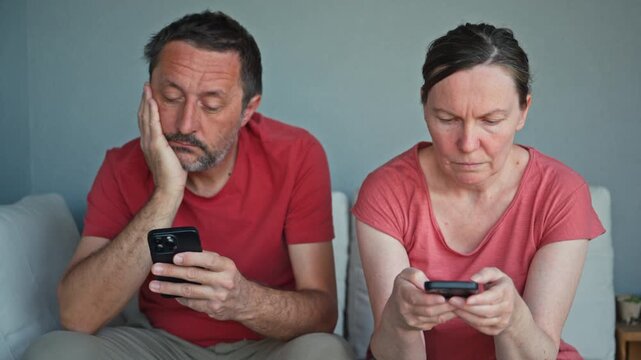 Couple using smartphones while sitting together outdoors, appearing bored and absorbed in separate screens. Relationship strain, technology dependence and lack of connection. 4K.