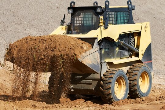 Yellow skid steer loader operating and scooping earth on a construction site with excavator