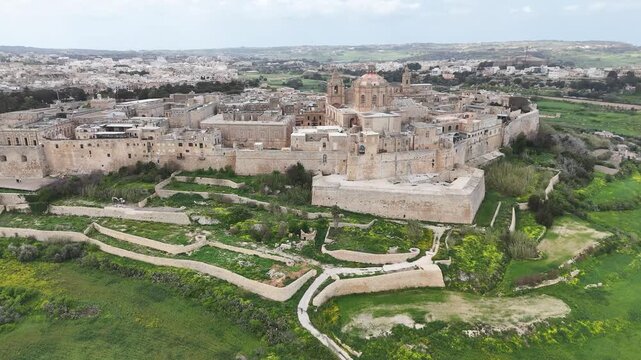 mdina bastion walls dry ditch gardens aerial view pathways ramparts fortress moat honey limestone st pauls cathedral dome skyline rabat malta silent city medieval citadel drone footage countryside