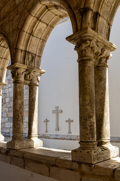 View of stone arches and columns of a historic cloister with three stone crosses embedded in the white wall in Estremoz, Evora District, Portugal.