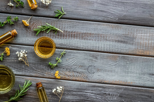 Natural wellness. Essential oils near herbs and leaves on dark wooden background top view pattern frame copy space