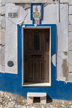 View of a traditional wooden door with blue painted trim and a decorative tile above in a stone wall in Estremoz, Evora District, Portugal.