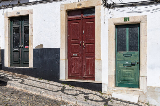 View of a traditional white building facade with three colorful doors and intricate black and white cobblestone pavement in Estremoz, Evora District, Portugal.