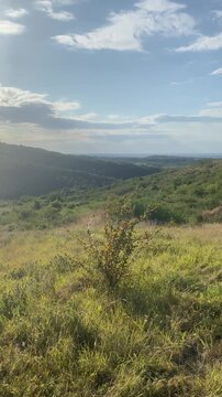 Slow pan across a scenic, rolling green hillside under a partly cloudy sky