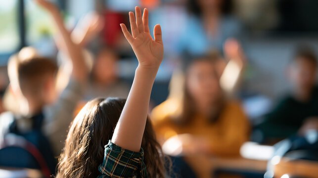 rear view of caucasian teen pupils raising their hands to answer a teacher's question during a bright classroom lesson, backs to camera, education and participation concept,