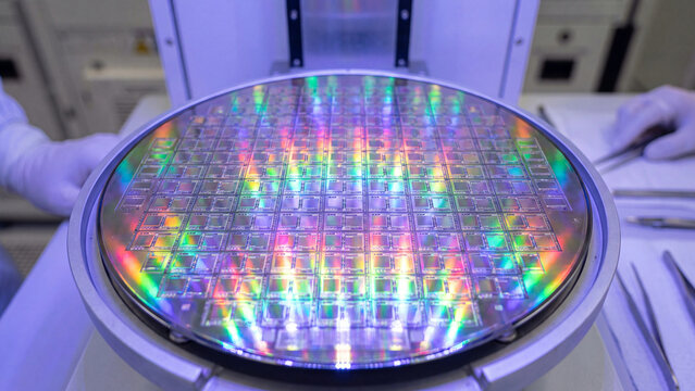 Silicon wafer reflecting vibrant rainbow diffraction colors during semiconductor manufacturing inspection.