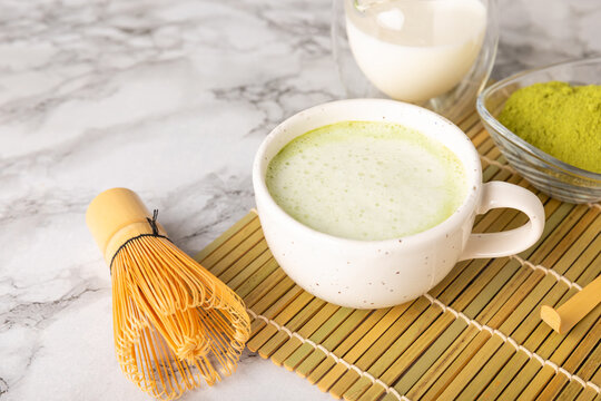 Fresh matcha latte in clear glass on the table with whisk and matcha powder. Iced matcha latte. Japanese green tea drink, creamy milk beverage, healthy antioxidant breakfast. minimal cafe style