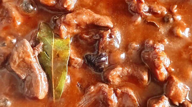 Slow cooking beef stew with rich gravy and bay leaf in a pan, close-up
